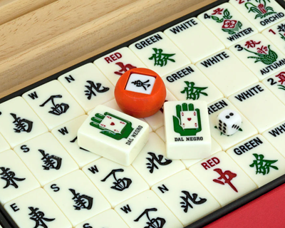 Mahjong game set with tiles, a red walnut piece, a dice, and Dal Negro hand tile on wooden background.